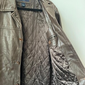 May include: Brown leather jacket with a button-up front and a quilted interior lining. The jacket has a classic collar and a tailored fit. The brand name "GAP" is visible on the label. The jacket is a medium size.