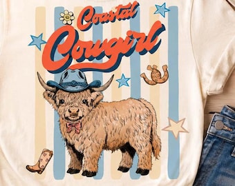 May include: Cream-colored t-shirt featuring a cartoon Highland cow wearing a cowboy hat and bow tie, with the text "Coastal Cowgirl". The design includes stars, a boot, and a flower. The shirt is styled with denim shorts and a cowboy hat.