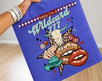 May include: A blue blanket with a graphic design featuring a skull, lips, playing cards, dice, a cowboy hat, and the text "baby I'm A Wildcard 777". The design includes a star, cherries, and hearts.
