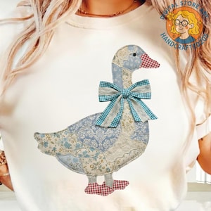 May include: A fabric goose applique featuring a patchwork design in blue and white floral patterns, a red and white checked beak and feet, and a blue gingham bow. This handmade item is likely a decorative piece.