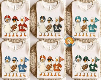 May include: White t-shirts featuring a cartoon illustration of three geese dressed in football attire. Each goose holds a football and wears a helmet or cap. One goose holds a flag that says "GO TEAM" and the number "01" is on the jerseys.
