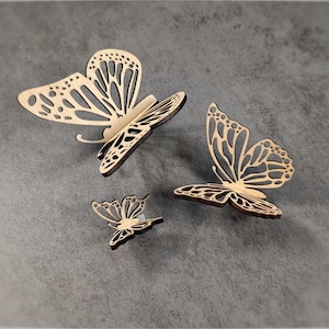 May include: Three wooden butterfly wall decor pieces in various sizes. The butterflies are cut out of wood and have a natural wood finish.