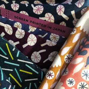 May include: Close-up of various fabric swatches with different patterns. One swatch has a navy blue background with white and pink circular designs. Another has a dark purple background with white circular designs. A label reads "SCREEN PRINTED IN JAPAN".