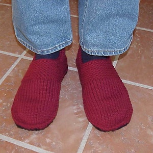 May include: A pair of red knitted slippers with a ribbed texture. The slippers are worn by a person wearing blue jeans.
