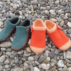 May include: Four knitted wool slippers, two teal blue and two orange, on a bed of small gray stones.