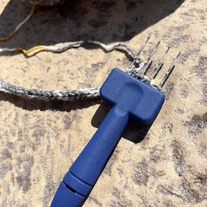 May include: A blue plastic knitting tool with five metal needles. The tool is used to create a loop stitch for knitting.