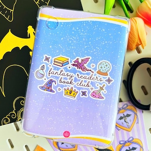 Op de afbeelding: Een doorzichtige tablethoes met een lichtblauwe en lavendelkleurige gradiënt. De hoes heeft een "Fantasy Readers Book Club" sticker met fantasie-illustraties, waaronder een draak, een drankfles en een tovenaars hoed. De hoes is ontworpen om de tablet te beschermen.