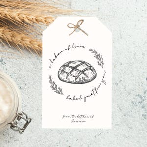 Op de afbeelding: Een wit cadeau-etiket met een handgetekend ontwerp van een brood. De tekst op het etiket luidt "a labor of love baked just for you from the kitchen of Summer".