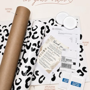K&ouml;nnte beinhalten: Eine braune Versandrolle aus Pappe, ein aufgerollter wei&szlig;er Vinylaufkleber mit schwarzem Leopardenmuster, zwei wei&szlig;e Kunststoffkappen, ein Lieferschein, eine Dankeskarte mit Anleitung und zwei wei&szlig;e Alkoholtupfer-P&auml;ckchen.