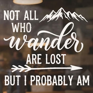 May include: A white vinyl decal featuring a mountain range graphic at the top and an arrow graphic in the middle. The text reads: NOT ALL WHO wander ARE LOST BUT I PROBABLY AM. The design uses a combination of block lettering and script typography.
