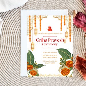 May include: A white invitation card with gold and orange accents. The card features a decorative archway with hanging lanterns and floral accents. The text reads "YOU'RE CORDIALLY INVITED TO THE Griha Pravesh Ceremony of our new home on 23TH MARCH, 2030 8:00 AM ONWARDS 123 Anywhere St., Any City, ST 12345".