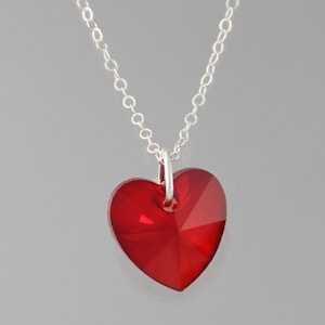 Może przedstawiać: Srebrny łańcuszek z czerwonym kryształowym sercem.