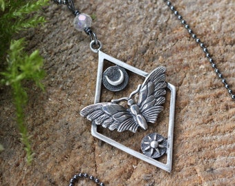 May include: A silver necklace with a pendant featuring a detailed butterfly design, a crescent moon, and a sun. The pendant is set in a diamond-shaped frame.