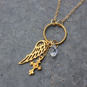 May include: Gold necklace with a twisted chain, a circular pendant, a crystal charm, a cross charm, and an angel wing charm.