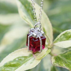 Op de afbeelding: Een zilveren ketting met een rode en zilveren geschenkdoos hanger. De geschenkdoos is versierd met heldere strass steentjes.