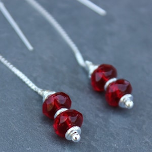 May include: A pair of silver dangle earrings with two red glass beads on each earring.