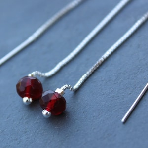 May include: A pair of silver chain earrings with red gemstone beads. The earrings are long and dangle.