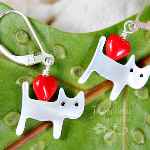 May include: A pair of silver earrings with white porcelain dog charms and red heart accents.