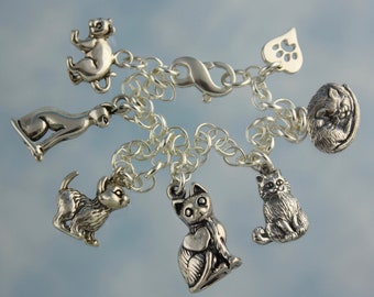 May include: A silver charm bracelet with multiple cat charms, including a sleeping cat, a sitting cat, a cat with a heart, and a cat with a paw print. The bracelet also has a heart charm with a paw print.