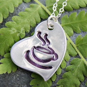 Könnte beinhalten: Eine silberne herzförmige Halskette mit einem Anhänger in Form einer violetten Kaffeetasse. Der Anhänger hängt an einer silbernen Kette.