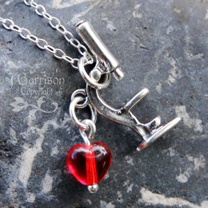 Puede incluir: Un collar de plata con un dije de microscopio y un dije de corazón de vidrio rojo.
