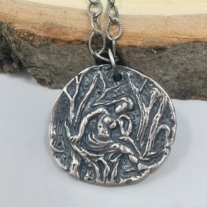 May include: A silver pendant necklace featuring a detailed, textured design of a woman holding a child within a circular frame.