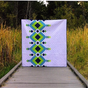 May include: A quilt pattern called "River Pond" by From Blank Pages, featuring a geometric design with blue, green, and white fabric. The quilt is displayed on a wooden walkway in a natural setting.