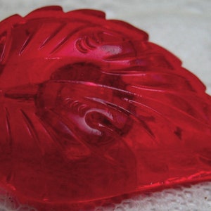 May include: A deep red glass leaf shaped paperweight with intricate carvings. The glass is translucent and has a glossy finish.