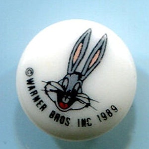 May include: A white button with a cartoon image of Bugs Bunny. The button has the text "Warner Bros. Inc. 1989" around the edge.