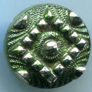 May include: A green glass button with a raised, silver-toned design. The button has a central circle surrounded by eight diamond-shaped points.