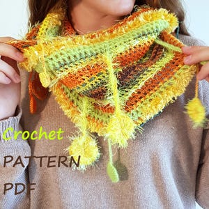 Puede incluir: Un cuello de ganchillo colorido en tonos amarillos, naranjas y verdes. El cuello presenta un diseño texturizado con detalles de hilo esponjoso y pompones colgantes. Las palabras "Crochet" y "PATTERN PDF" son visibles.