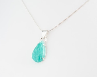 May include: A silver necklace with a teardrop-shaped pendant. The pendant has a light turquoise gemstone set in a silver bezel. The necklace hangs on a fine silver chain. The background is plain white.