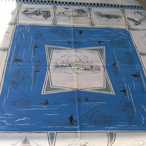May include: A white tablecloth with a blue and white pattern. The pattern features boats, nets, and buildings. The tablecloth has a scalloped edge.