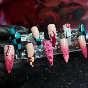 Puede incluir: Un conjunto de diez uñas artificiales largas en forma de almendra. Los diseños incluyen una llama rosa y roja, un patrón geométrico rosa y un patrón de cuadros negros y verde azulado. Otras uñas presentan un degradado de nude a rosa.