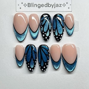 May include: A set of ten artificial nails. The nails feature a variety of designs, including a light pink base with a teal glitter French tip and a butterfly wing design in black and teal glitter. The text "Blingedbyjaz" is at the top.