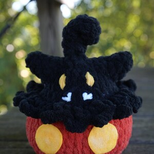 Puede incluir: Un peluche de ganchillo hecho a mano con forma de personaje de dibujos animados. El juguete presenta un cuerpo rojo con dos c&iacute;rculos amarillos, una cabeza negra con detalles amarillos y blancos y una parte superior rizada. El peluche est&aacute; hecho de hilo suave.