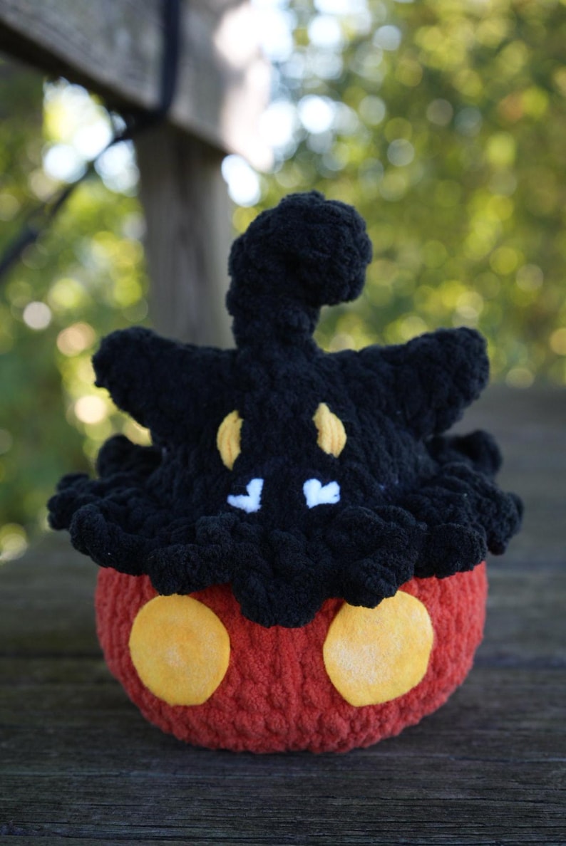 Puede incluir: Un peluche de ganchillo hecho a mano con forma de personaje de dibujos animados. El juguete presenta un cuerpo rojo con dos c&iacute;rculos amarillos, una cabeza negra con detalles amarillos y blancos y una parte superior rizada. El peluche est&aacute; hecho de hilo suave.