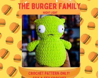 May include: Green crocheted plush toy with large eyes and a small mouth. The toy is shaped like a human figure and is holding its arms out. The toy is sitting on a hand. The background is a yellow pattern of cartoon hamburgers. The text "THE BURGER FAMILY NIGHT LIGHT CROCHET PATTERN ONLY! FOX & FEY CROCHET" is at the top of the image.