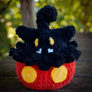 Puede incluir: Un peluche hecho a mano con ganchillo con forma de personaje de dibujos animados. El juguete presenta una cabeza negra con detalles amarillos y un cuerpo rojo con dos grandes c&iacute;rculos amarillos. El peluche est&aacute; hecho de hilo suave.