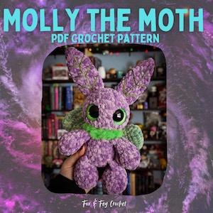 Peut inclure: Une peluche en crochet violet représentant un papillon de nuit, avec de grands yeux expressifs et des détails verts. Le papillon a de grandes oreilles en forme de feuilles et un col vert. Le texte "MOLLY THE MOTH PDF CROCHET PATTERN" est affiché en haut, avec "Fox & Fey Crochet" en bas.