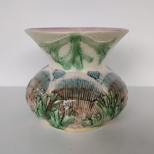 May include: A decorative ceramic vase with a bulbous base and flared top. The vase features a textured surface with green, blue, and brown leaf and shell-like patterns. The rim is a soft pink color, and the vase is approximately 8 inches tall.