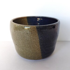 May include: A small ceramic bowl with a speckled green glaze on one side and a dark blue glaze on the other side.