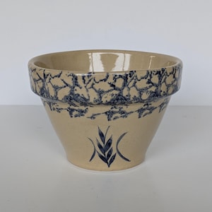 May include: A beige stoneware bowl with a blue, crackled pattern around the rim and a stylized wheat design. The bowl has a wide opening and a slightly tapered shape, suitable for serving or display.