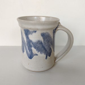 May include: A white ceramic mug with a blue and white abstract design. The mug has a rounded handle.