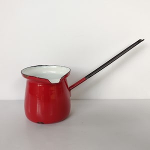 May include: Red enamel coffee pot with a black handle. The pot has a white interior and a rounded shape.