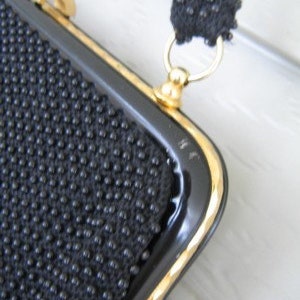May include: A black beaded evening bag with a gold clasp and chain strap. The bag has a black patent leather trim.