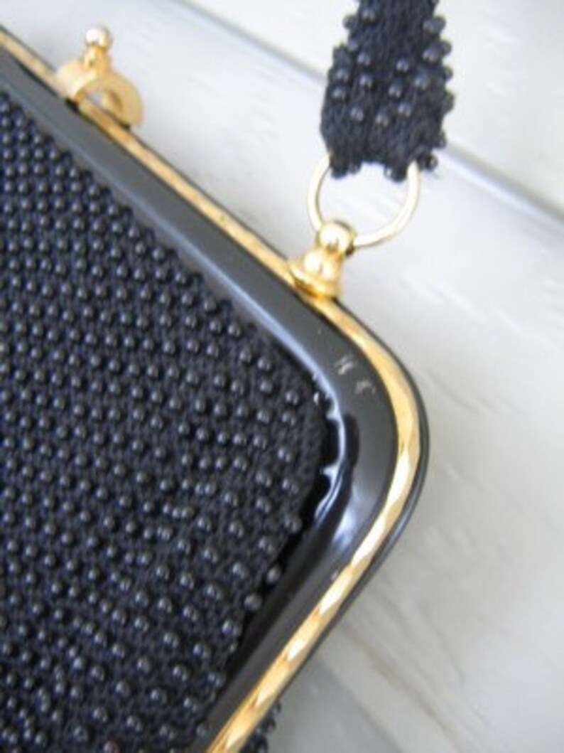 May include: A black beaded evening bag with a gold clasp and chain strap. The bag has a black patent leather trim.