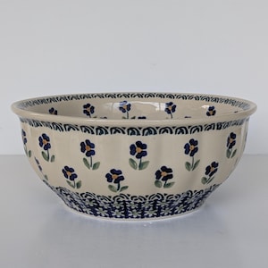 May include: A ceramic bowl with a cream-colored base, adorned with a repeating pattern of blue floral designs and green leaves. The rim and base feature intricate blue patterns. This decorative bowl is suitable for serving or display.
