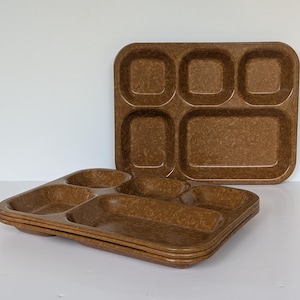 May include: A stack of rectangular brown cafeteria trays with a mottled texture. Each tray features five distinct compartments, including three smaller square sections at the top and two larger rectangular sections at the bottom for food items.