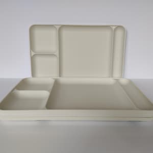 Pode incluir: Bandeja de servir retangular creme dividida com vários compartimentos. A bandeja está aberta, revelando uma pilha de bandejas semelhantes abaixo. Os compartimentos variam em tamanho e forma, projetados para controle de porções ou organização de alimentos.
